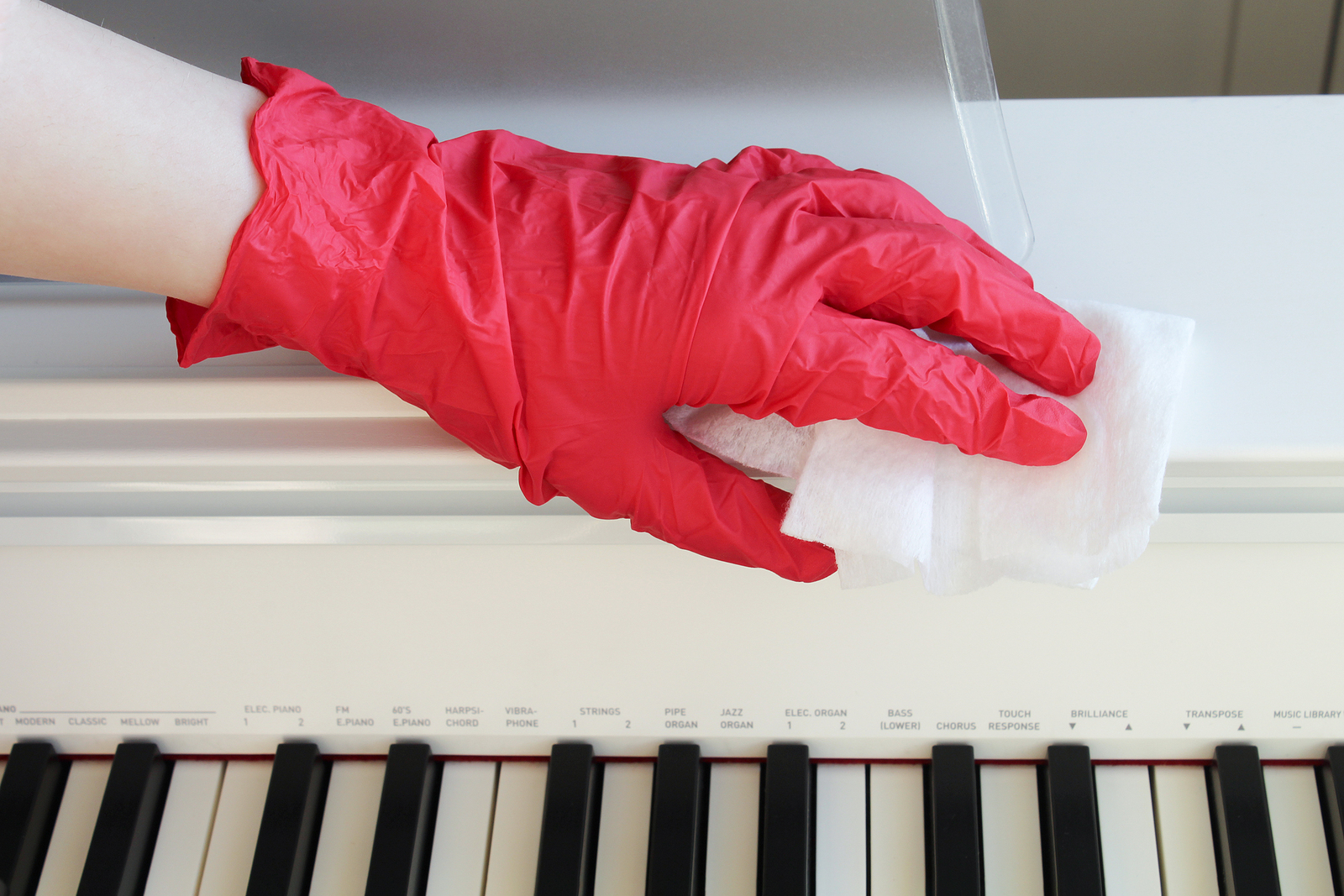 una mano con guanto pulisce un pianoforte durante la sanificazione di un ambiente di lavoro